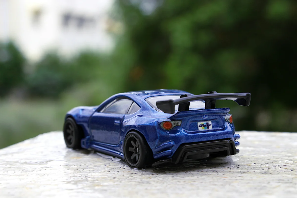 Diecast coupe biru dengan sayap belakang besar, difoto dari belakang
